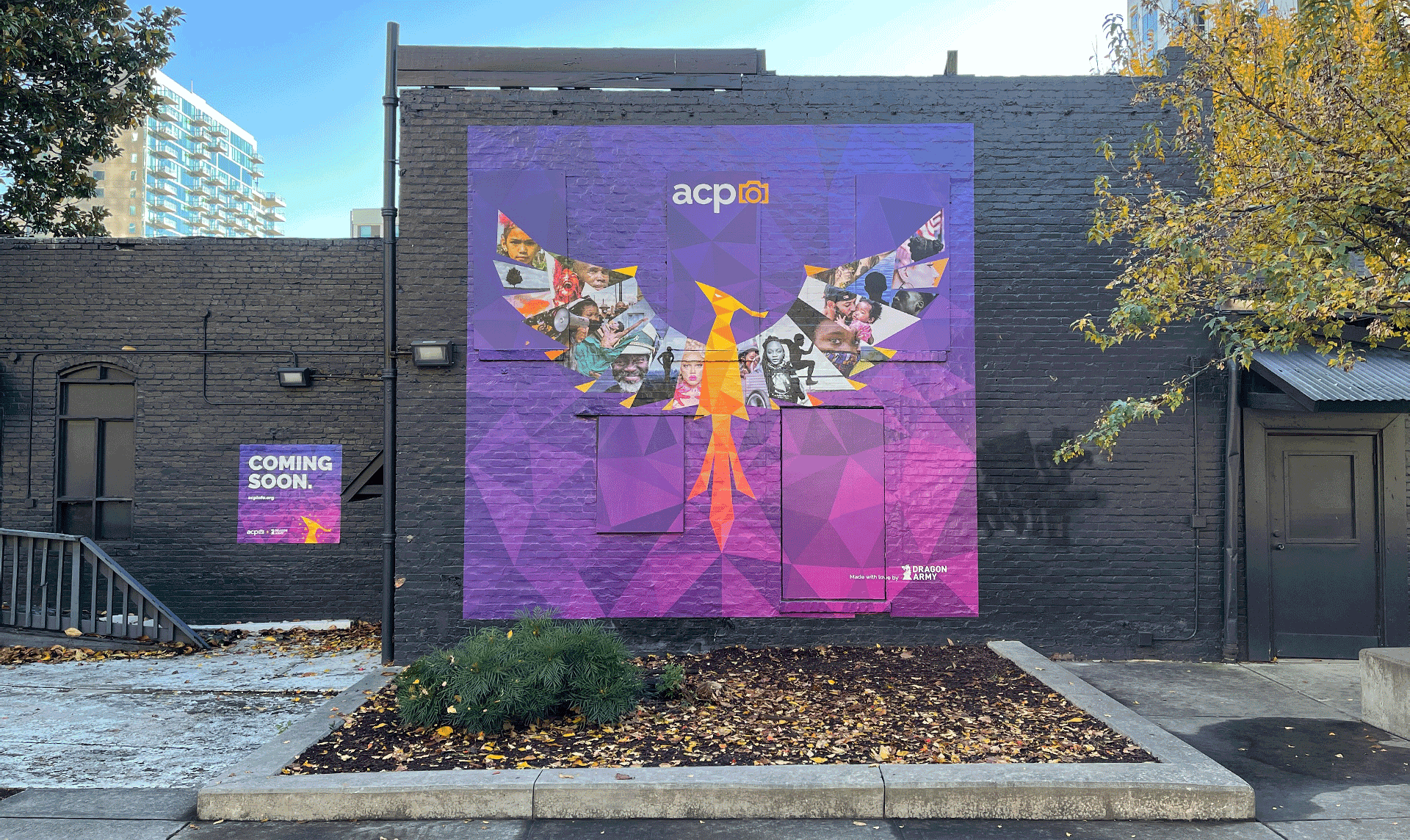 Purple and gold phoenix mural installed on a charcoal grey, exterior building wall.